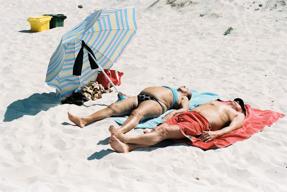 昼間に青と白のビーチパラソルに横たわる赤いビキニの女性