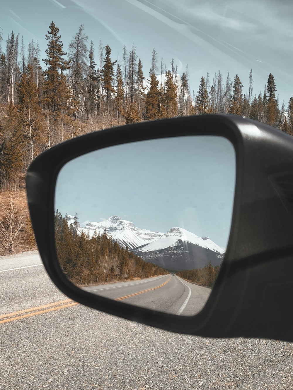 Espejo lateral del coche que muestra la montaña cubierta de nieve