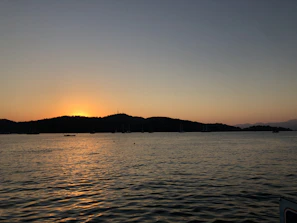 Sunset view over the water with silhouettes of sailboats and crew members