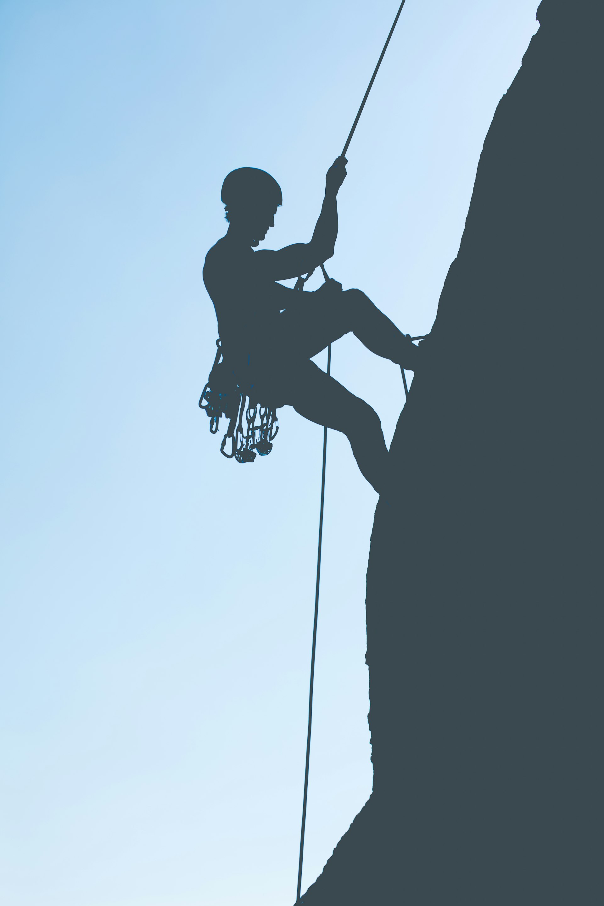 The silhouette of a rock climber against a pale blue sky.