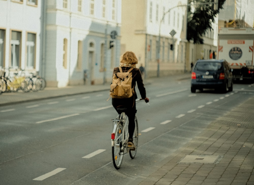 昼間、道路を自転車で走る黒いジャケットの女性