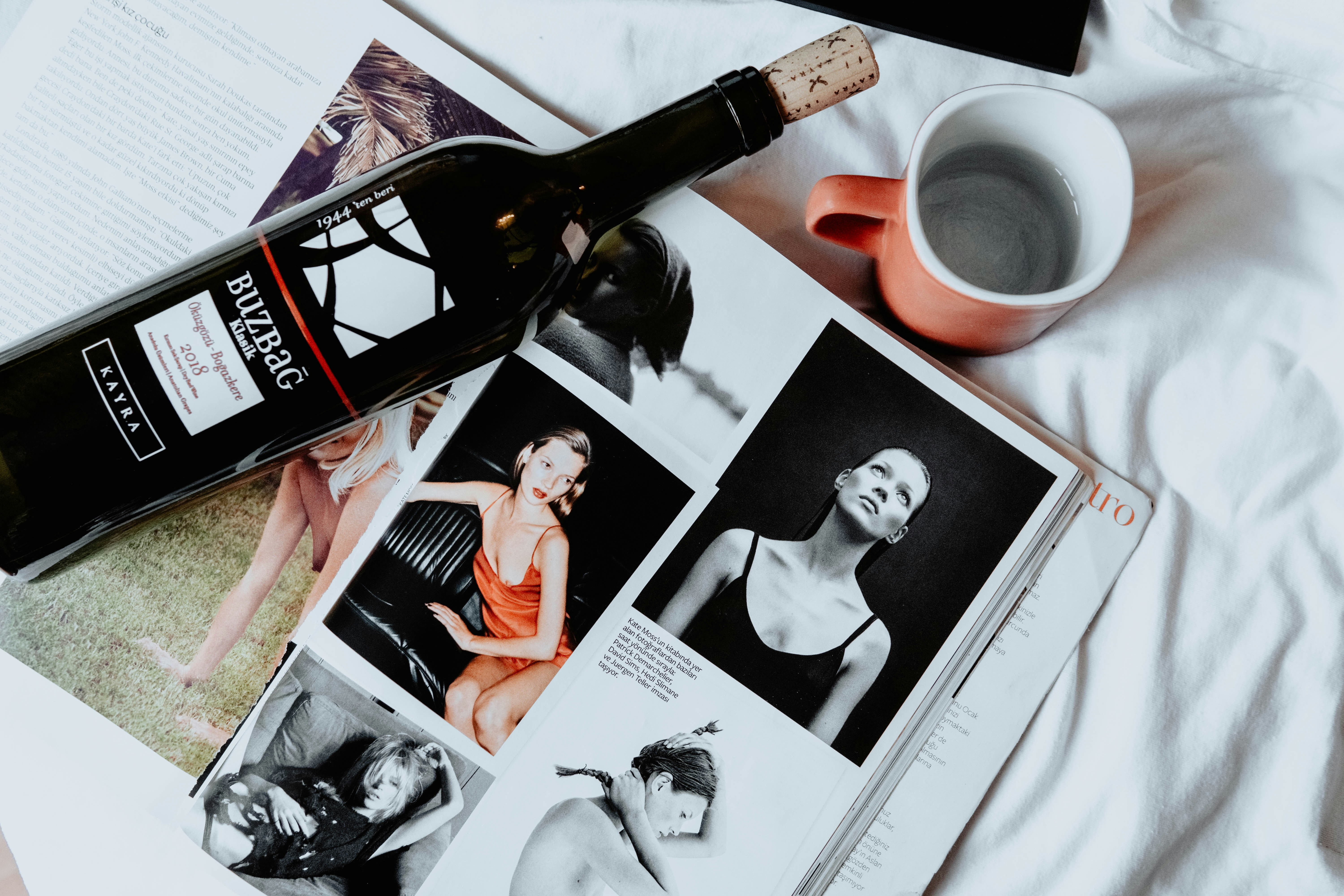 uma garrafa de vinho sentada em cima de uma revista ao lado de uma xícara de café