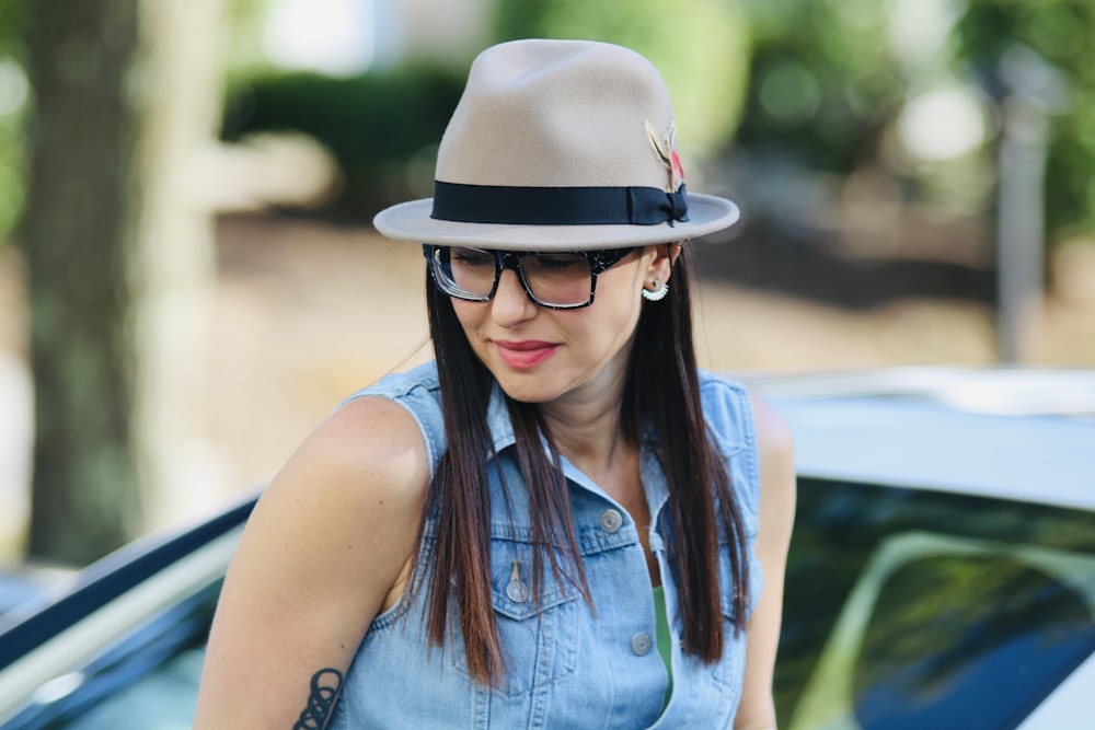 a woman wearing a hat and glasses standing next to a car