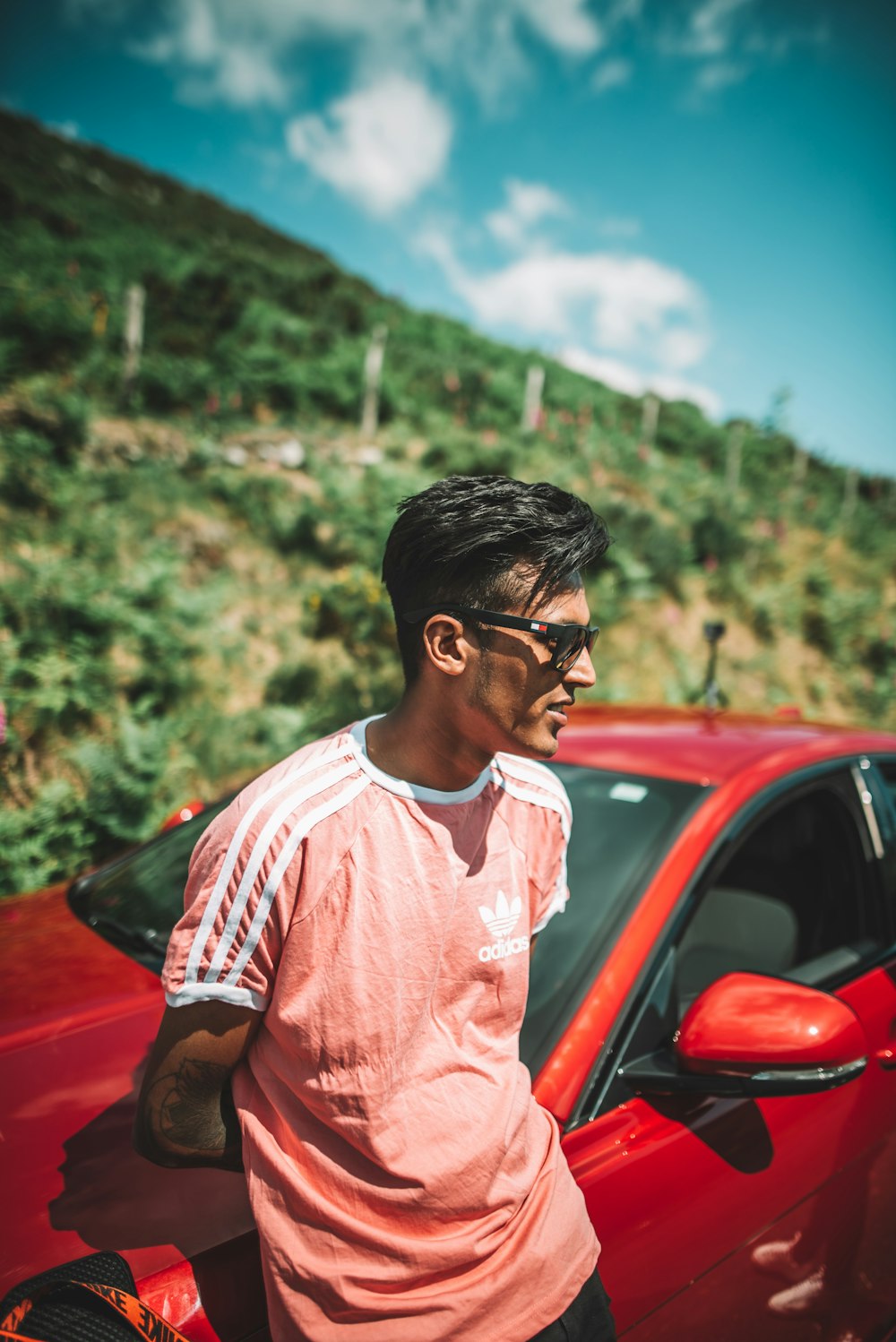 man in white and red crew neck t-shirt standing beside red car during daytime