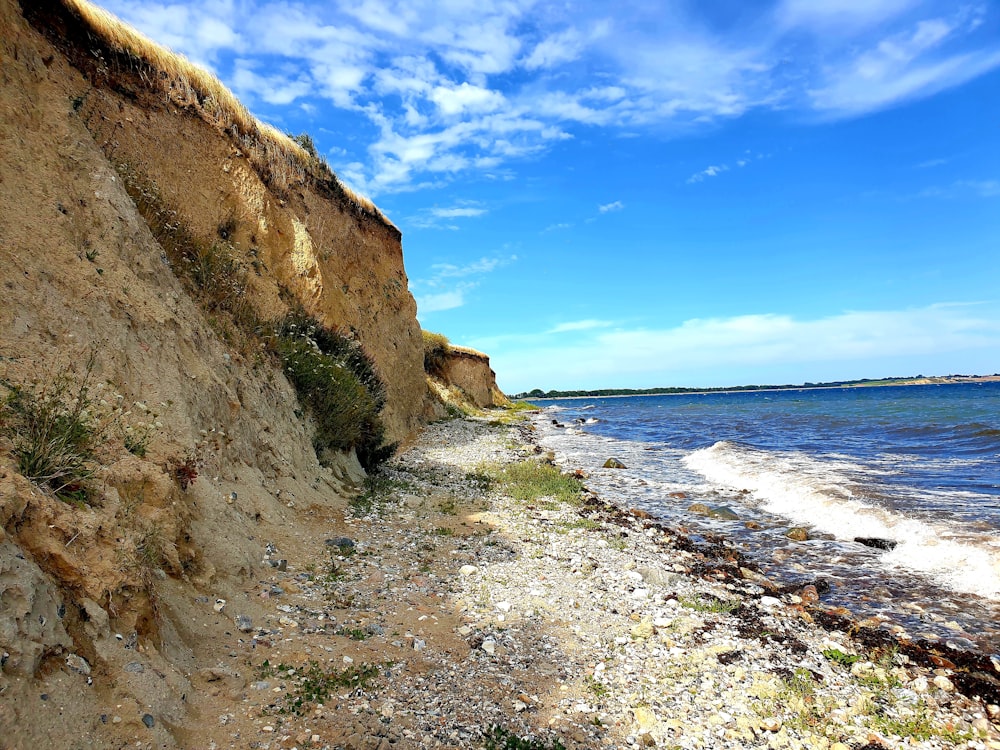 brown rocky mountain beside sea under blue sky during daytime