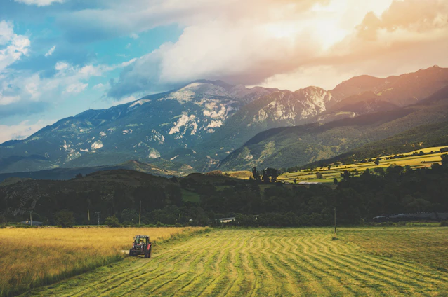 A panoramic drone shot capturing lush farmland with tractors working under a clear blue sky.