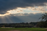 Sunlight breaking through clouds over a lush, green landscape.