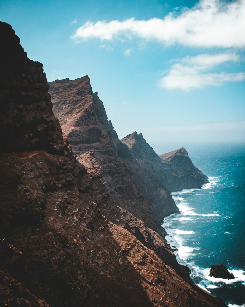 brown rocky mountain beside sea during daytime