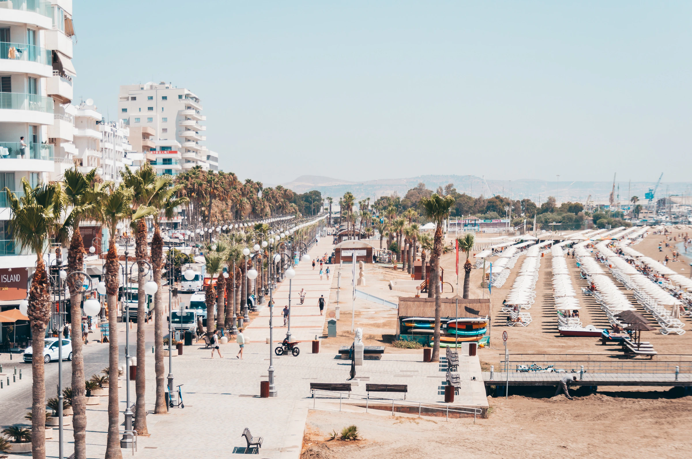 Sunbathers on the sandy shore of Larnaca's palm-lined seafront with the town behind