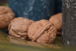 Close-up of plump walnuts resting on a rustic wooden table with mountain scenery blurred in the background.