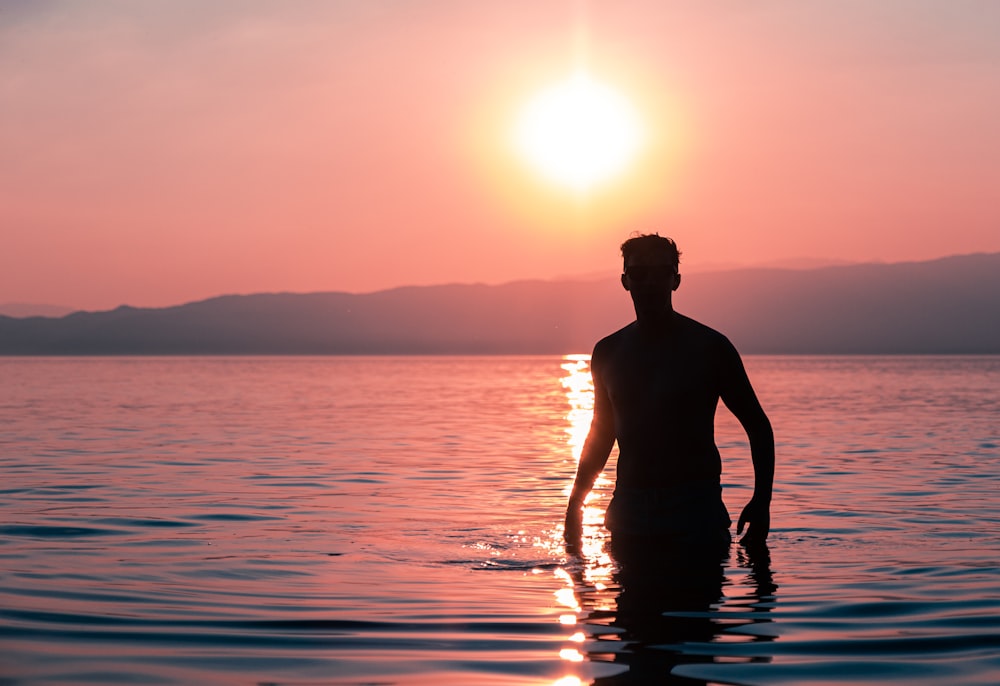 silhouette of man standing on water during sunset