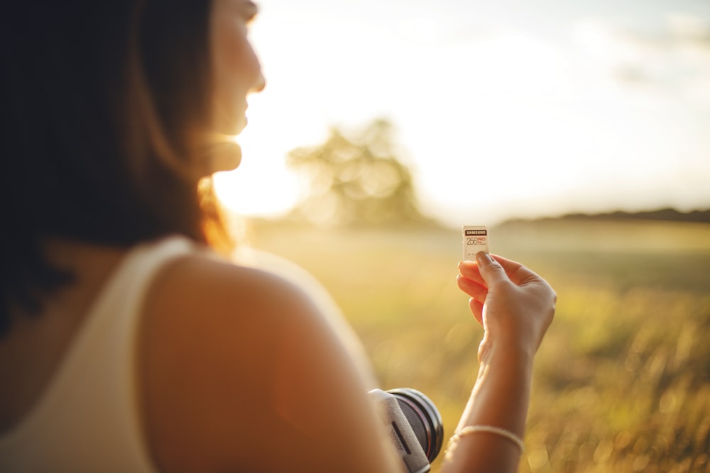 Femme en débardeur blanc tenant une bouteille en plastique blanche et orange pendant le coucher du soleil