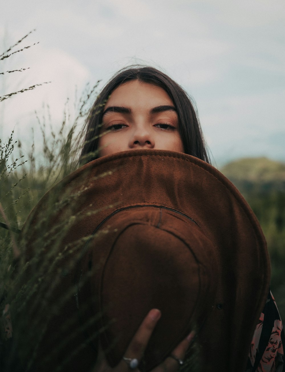 낮 동안 푸른 잔디 근처에 서 있는 갈색 모자를 쓴 여자