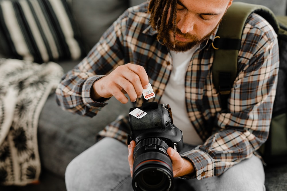 man in brown and white plaid dress shirt holding black nikon dslr camera