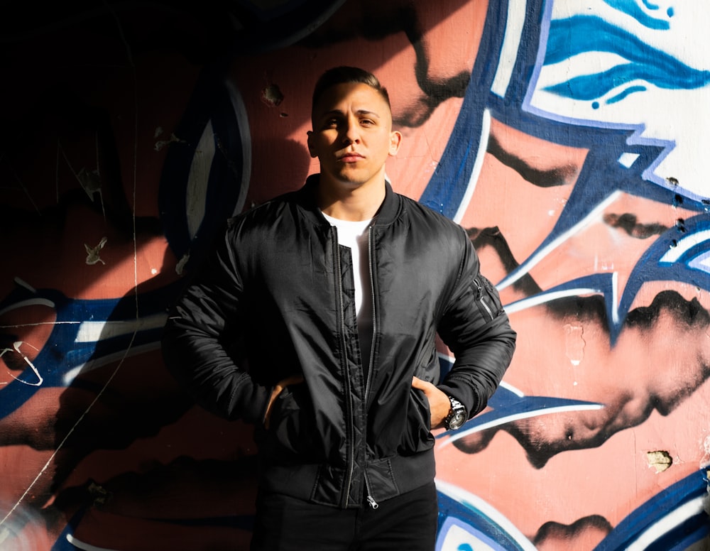 man in black leather jacket standing beside wall with graffiti