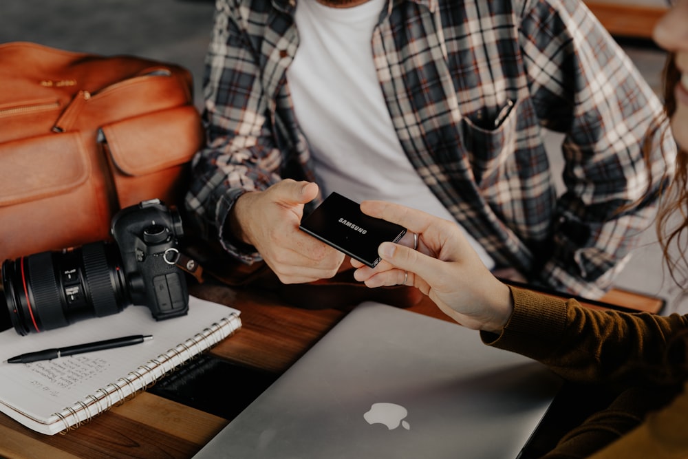 uomo in camicia a quadri bianca e nera che tiene lo smartphone nero