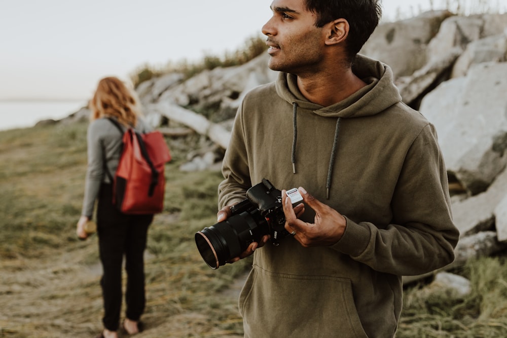 man in gray hoodie holding black dslr camera