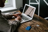 person in gray long sleeve shirt using macbook air on brown wooden table