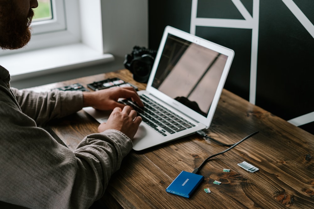 Personne en chemise à manches longues grise utilisant MacBook Air sur une table en bois marron