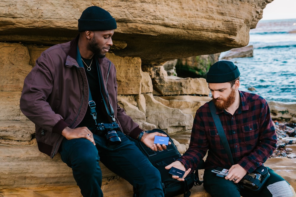 uomo in giacca nera e jeans blu in denim seduto sulla roccia