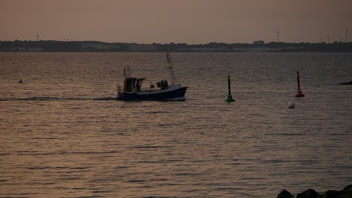A fishing boat equipped with a GPS device sailing on calm waters at sunset.
