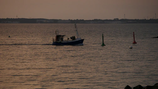 A sleek fishing boat cutting through the calm waters of Daugava river at sunset.