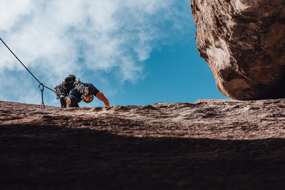 man in black jacket and orange pants climbing on brown rock mountain during daytime