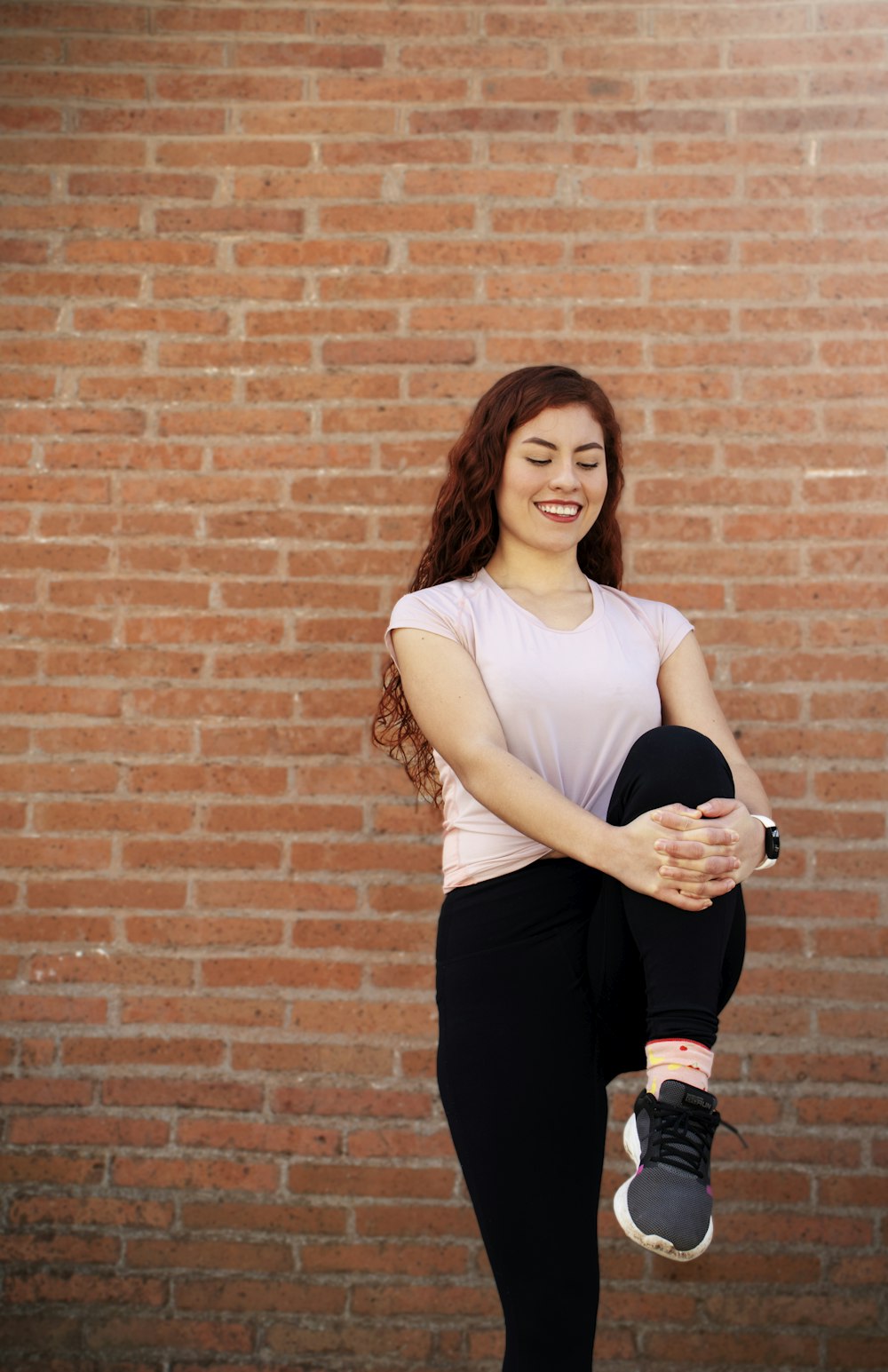 woman in white tank top and black pants standing beside brown brick wall
