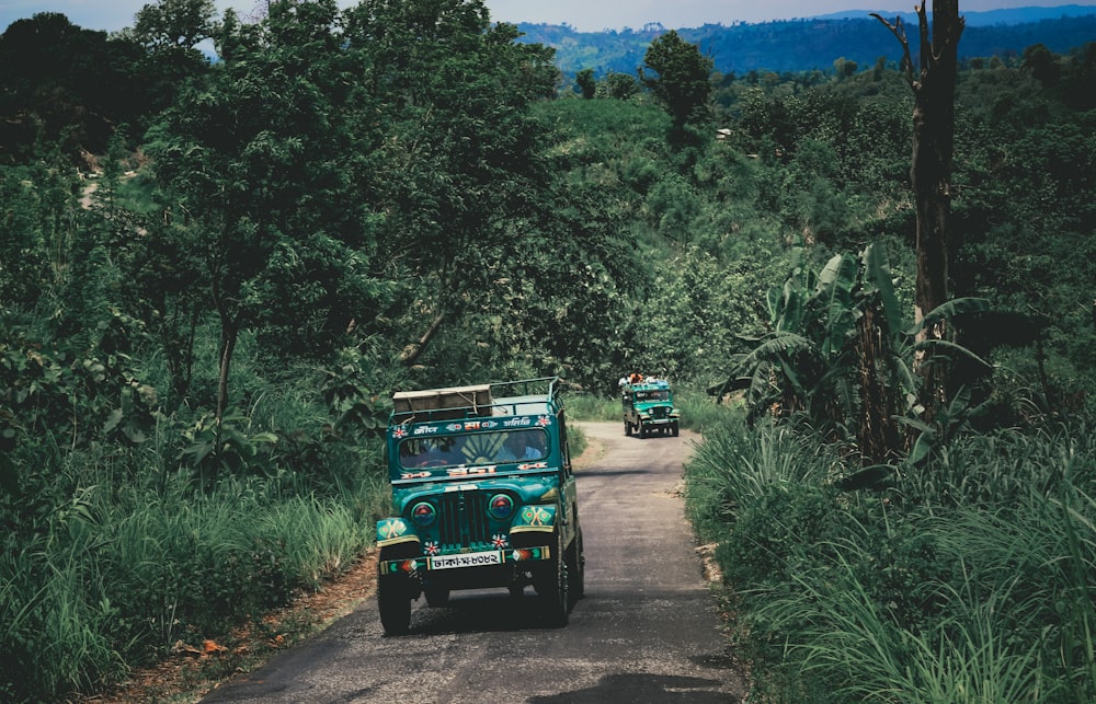 Jeep Wrangler bleue sur un chemin de terre entouré d’arbres verts pendant la journée