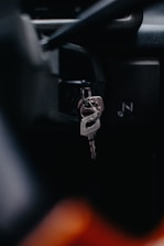 A close-up view of a car's ignition switch with keys inserted. The focus is on the metal keychain and key, with a blurred background that suggests a vehicle interior.