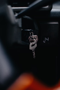 A close-up view of a car's ignition switch with keys inserted. The focus is on the metal keychain and key, with a blurred background that suggests a vehicle interior.