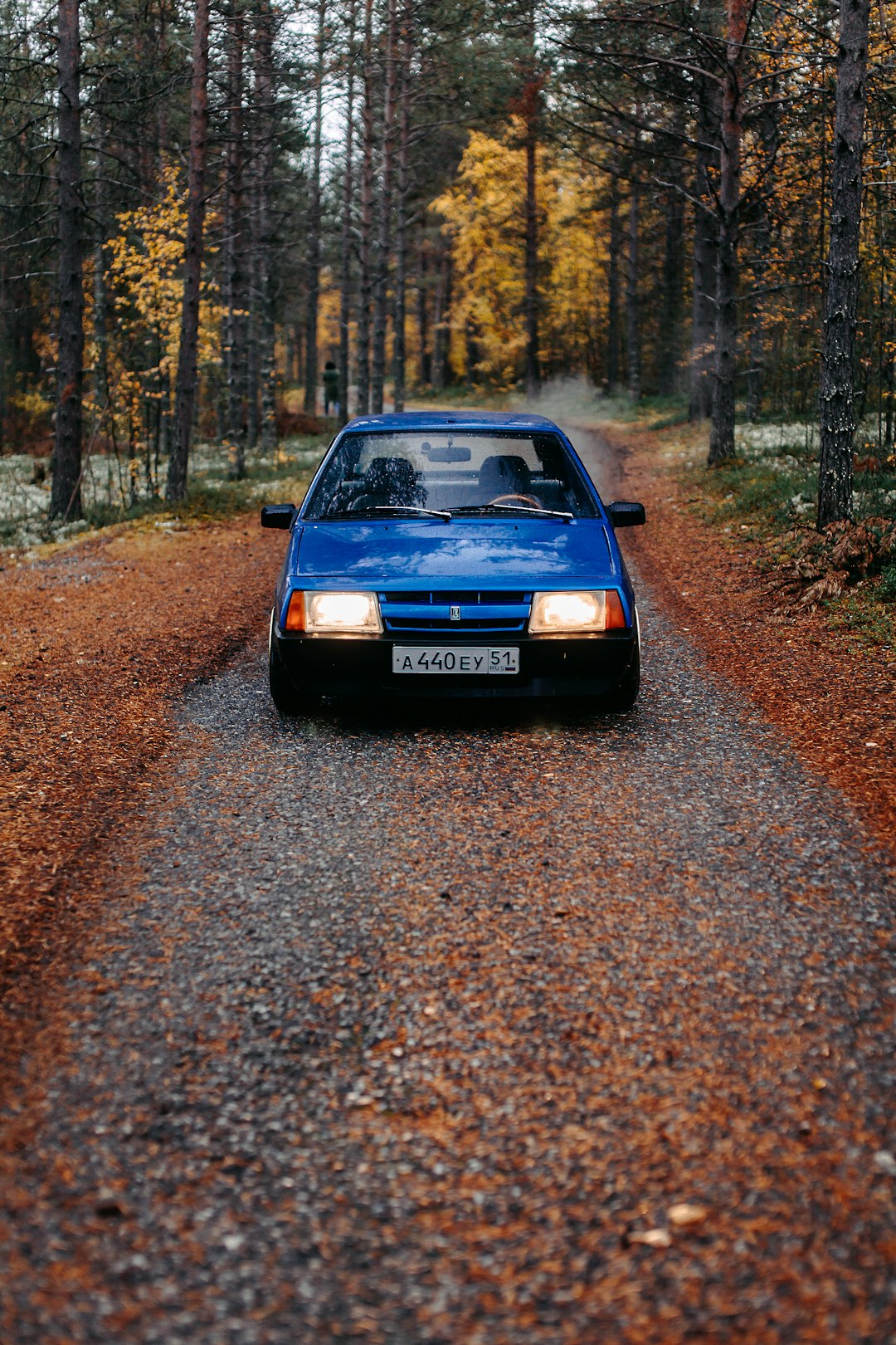 blue car on dirt road in between trees during daytime