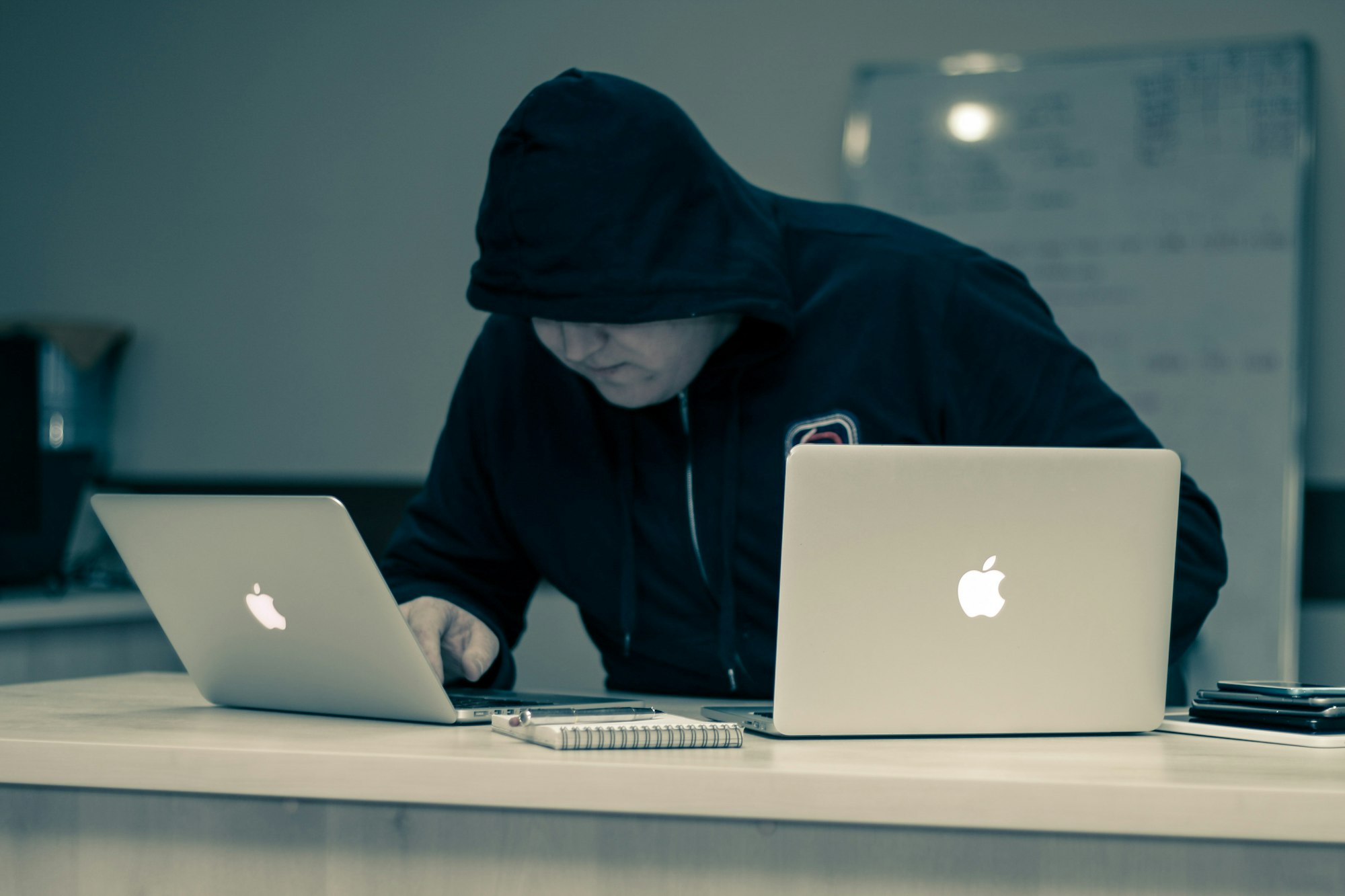 A man covered in hoody with PCs on a desk