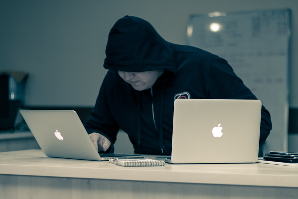 黒いパーカーを着た男がMacBookを使って