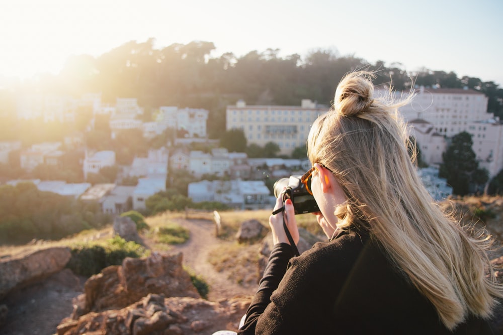 woman in black coat taking photo of city during daytime