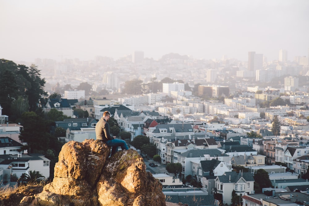 woman in blue long sleeve shirt sitting on brown rock during daytime