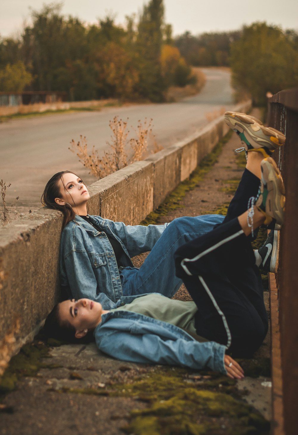 woman in blue denim jacket lying on concrete wall during daytime