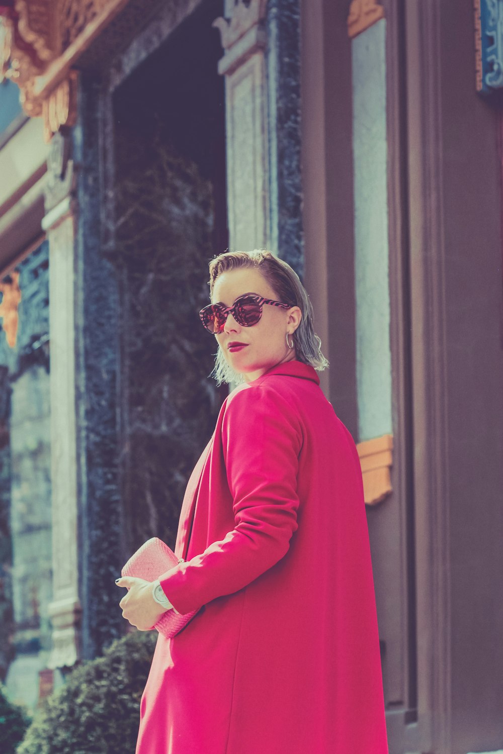 woman in red long sleeve shirt wearing sunglasses standing near brown wooden door during daytime