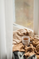 A cozy morning scene with a person enjoying Cristine coffee by a window with soft beige curtains.