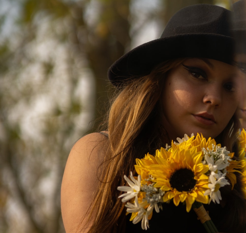 woman in black hat holding yellow sunflower