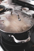 Close-up of a large purple pot with a shiny lid, steam gently rising as it simmers on a stove.
