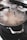 A large metal pot with a speckled surface and stainless steel handles is positioned on a stove. The lid is slightly fogged, indicating that the contents may be steaming or hot. In the background, there are blurred kitchen objects, including two white bowls and another pot.