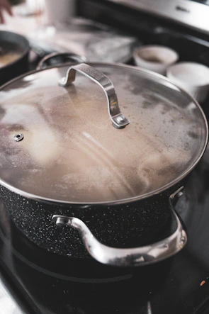 Close-up of a large purple pot with a shiny lid, steam gently rising as it simmers on a stove.