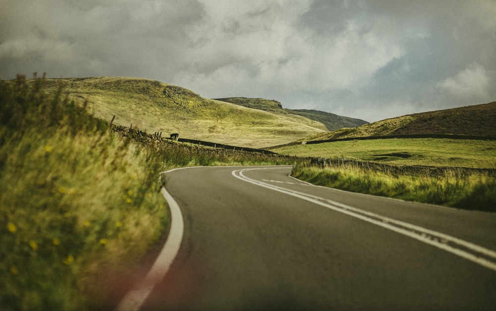 gray asphalt road between green grass field under gray cloudy sky during daytime