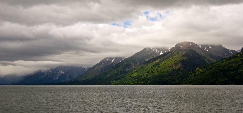 green mountain beside body of water under cloudy sky during daytime