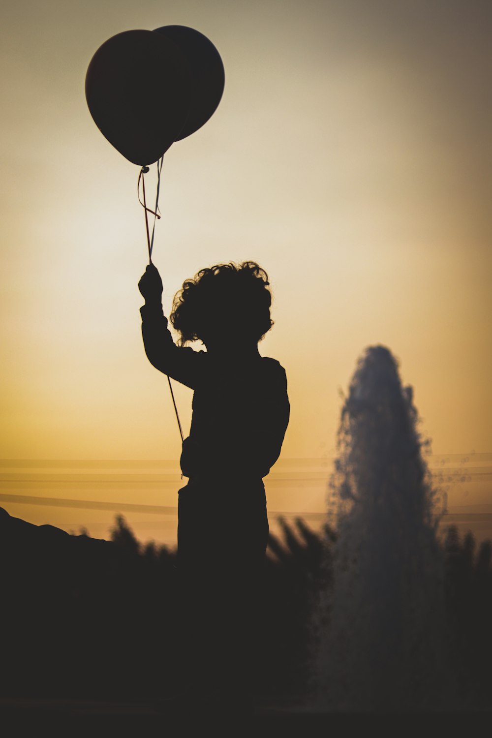 Silhouette eines Mannes, der während des Sonnenuntergangs einen Herzballon hält
