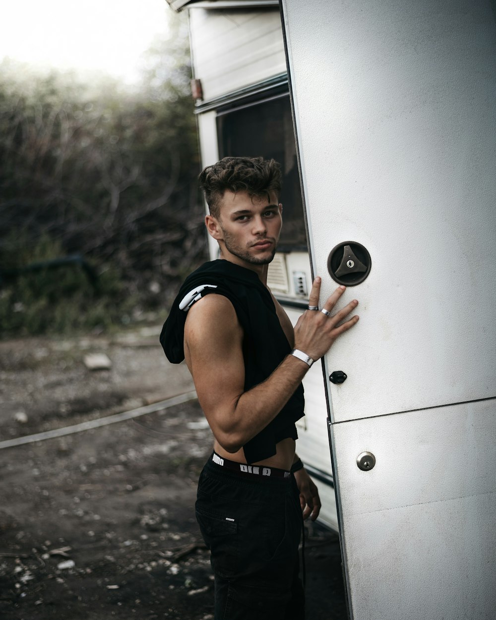 man in black tank top and black pants leaning on white wall