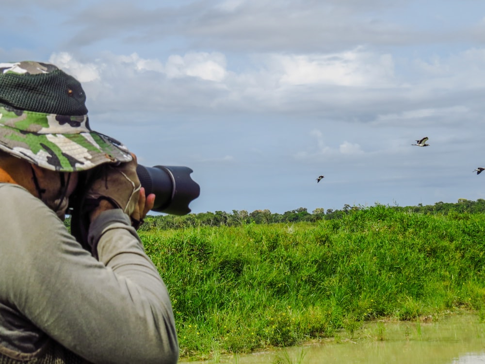 Mann in grauer Jacke und schwarzer Hose fotografiert tagsüber ein grünes Grasfeld