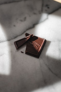 Close-up of a hand breaking a glossy, dark chocolate bar with visible cocoa nibs.