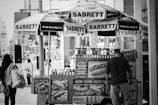 A bustling city street scene with a Sabrett Select vendor serving happy customers on a sunny day.
